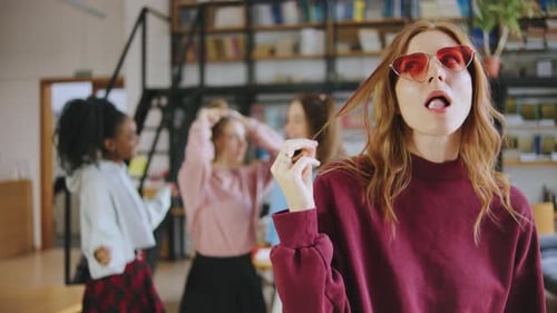 Friends are Gathered in a Classroom Setting Chatting and Laughing One Redhaired Student is Blowing a