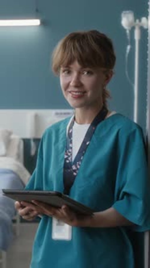Vertical Portrait of Cheerful Young Nurse with Digital Tablet in Hospital Ward