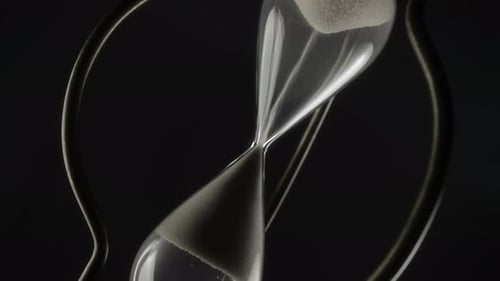 Hourglass with pouring sand rotating on black background. Abstract