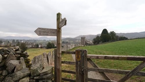 Wooden trail sign where the nature path splits into two. Showing church and farmland in the distance