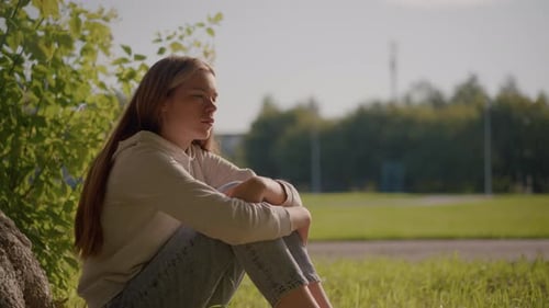 Contemplative Woman Sitting on Grassy Field with Sunlit Peaceful Background