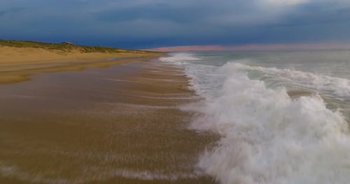 A Drone Flies Over the Ocean's Breaking Wave at Sunset