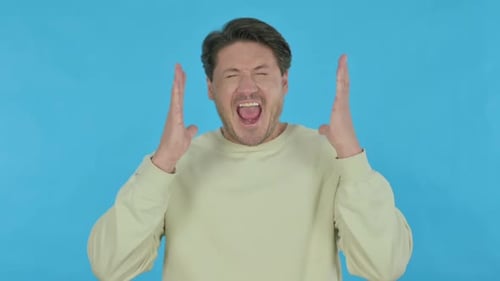 Young Man Screaming in Frustration on Blue Background