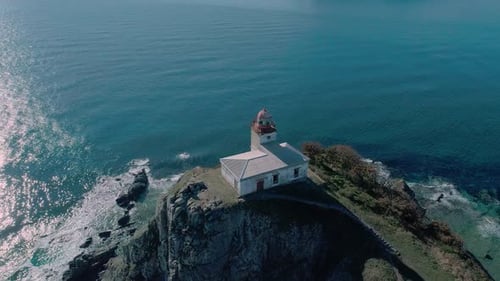 Aerial Panoramic View of White Lighthouse on the Rocky Cliff at Seaside Waves are Crashing to the