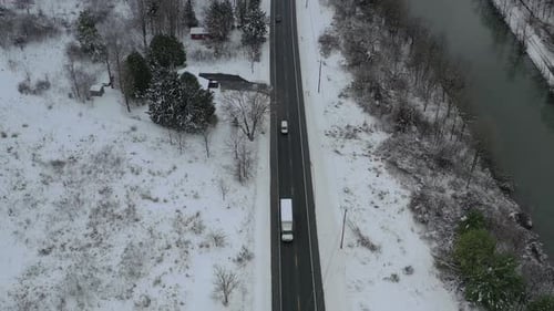Bird's eye view of white truck and other vehicles traveling down a highway next to a river in winter