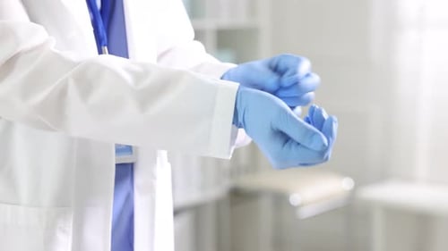 Doctor putting on medical gloves in hospital, closeup