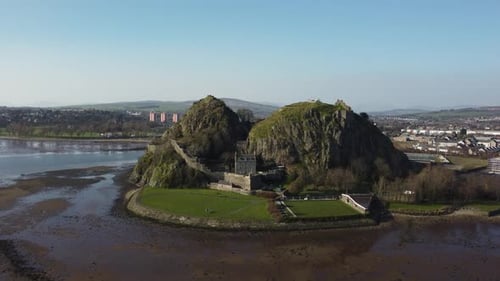 An aerial view of a historic rock fortress surrounded by water and lush greenery. The scene showcase