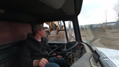 Heavy tractor loading vintage dump truck while driver, interior view