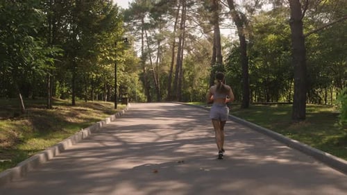 Woman Running Through Sunny Park on Paved Road
