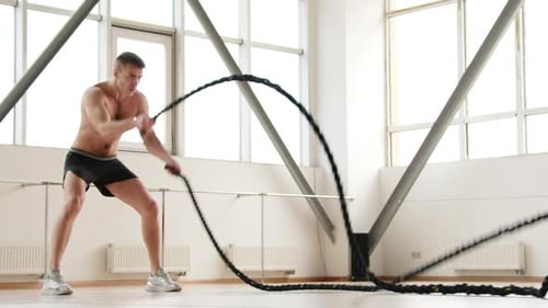 Muscular Man Doing Battle Rope Exercise in Gym
