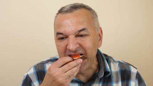 64. A man is eating a sandwich with vegetables while sitting at the table.