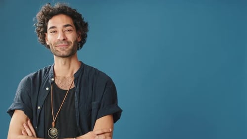 Smiling man points to side to show advertising space isolated on blue background in studio