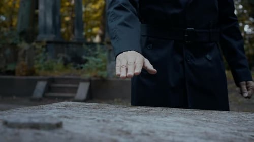 Nahaufnahme eines Mannes, der auf dem Friedhof spaziert und die Hand auf den Grabstein legt