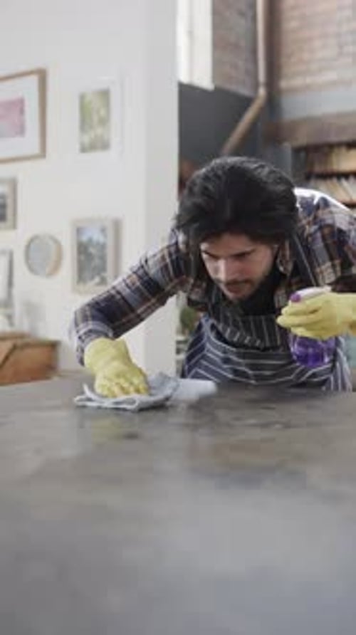 Vertical video of biracial man cleaning worktop in kitchen, slow motion