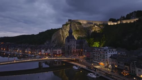 Cars Drive Over a Bridge in Dinant Belgium The Citadel is Illuminated on the Cliff Above the Meuse