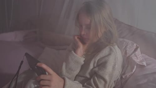Girl Plays Handheld Game in Bed at Night