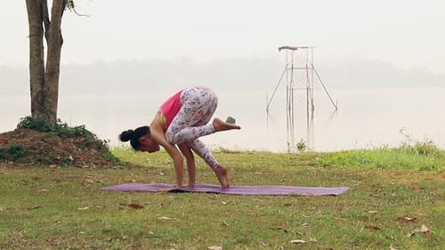 Femme asiatique pratiquant le yoga à Bakasana ou Frog Pose dans un parc extérieur.