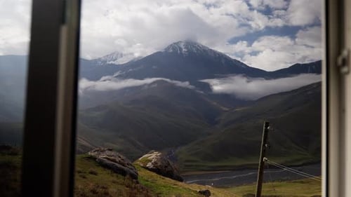 Sunlight Illuminates a Green Valley with a Lake As Clouds Move Revealing a Snowcapped Mountain Peak