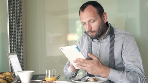 Homme d'affaires travaillant avec une tablette et un ordinateur portable pendant le petit déjeuner à la maison pour adultes