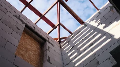 Niedrigwinkelaufnahme eines hölzernen Dachrahmens über unfertigen Hauswänden mit Schatten werfendem Sonnenlicht, auffällig