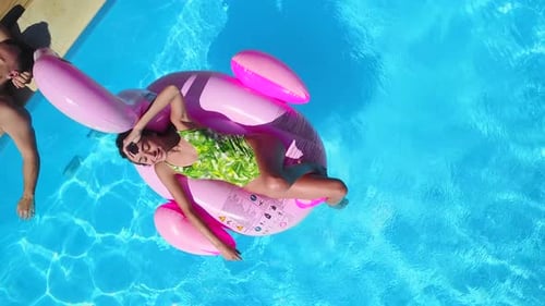 Aerial Girl Chilling on Inflatable Pink Flamingo Float in Swimming Pool Man Relaxing Tanning at
