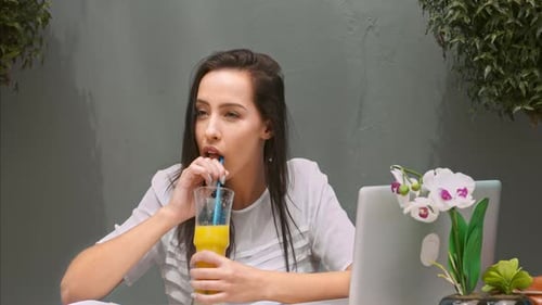 Woman Drinking Juice Near Laptop and Smiling