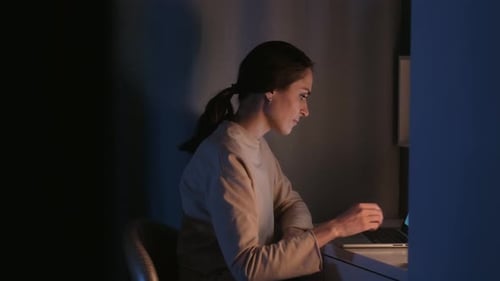 Young Woman Using Phone and Laptop at Desk