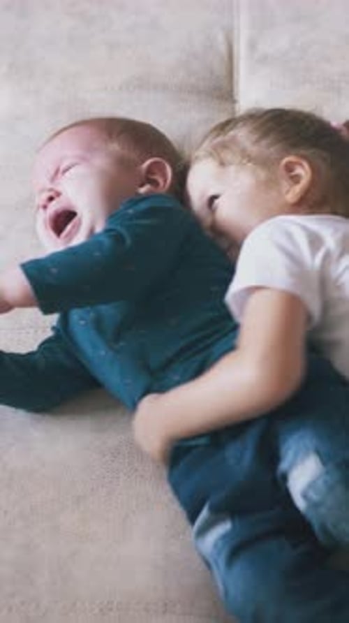 Little Girl Hugging Crying Infant on Sofa
