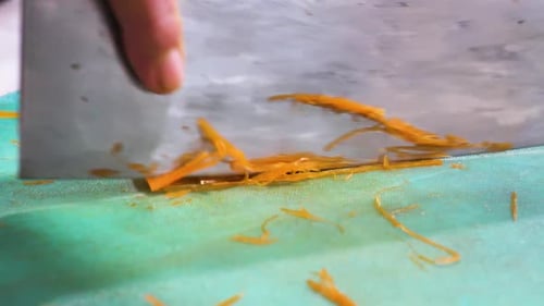 Close-up of a sharp knife slicing a carrot with precision, sending thin orange shavings flying.