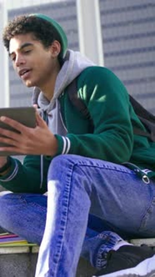 Vertical video: Holding tablet, student with beanie sharing screen, speaking on steps with backpack