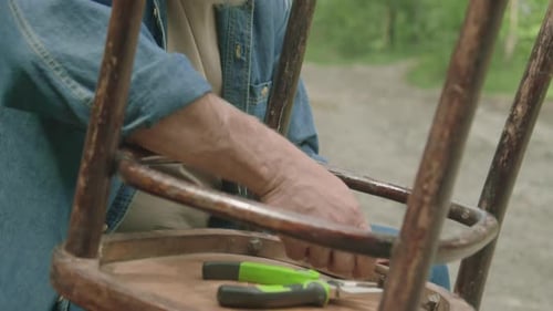 Old Man Repairing Chair while Spending Time Outdoors