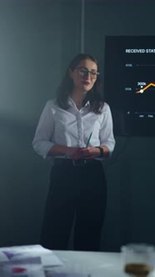 Confident Businesswoman Giving Datadriven Presentation to Colleagues in Dim Conference Room with