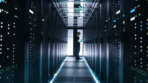 Un
ingeniero de TI masculino trabaja en una computadora portátil en un centro de Big Data. Se ven filas de servidores en rack.