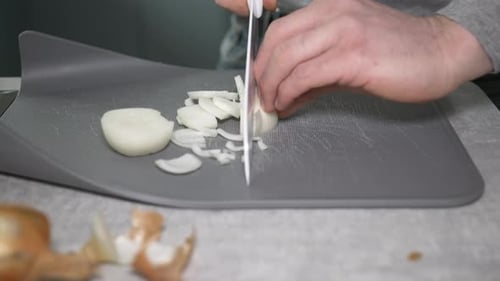 A man chopping onions in a home kitchen on a chopping board.