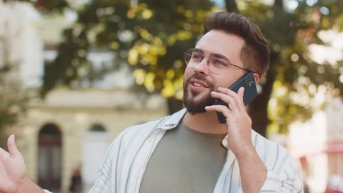 Happy Young Caucasian Man Tourist in Casual Talking on Smartphone While Standing on City Street