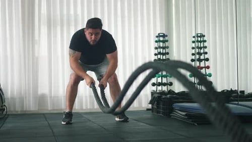 Man Using Battle Ropes For Whipping Exercise in a Gym in slow motion