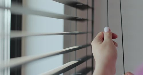 Close Up Woman Opens Blinds in Dark Room Stretches Sunlight Behind Horizontal Blinds Metal Blinds