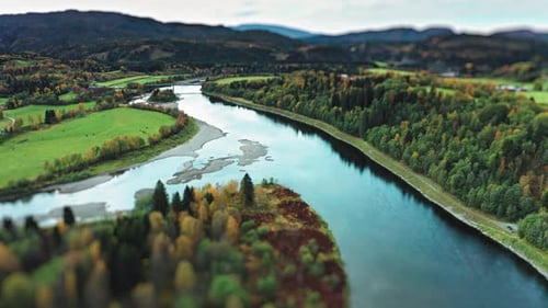 The landscape is a blend of vibrant farm fields and autumn forests, with a winding river leading the