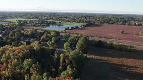 Vorwärts fahrende Luftdrohne über einem landwirtschaftlichen Feld neben einer Autobahn mit Blick auf einen See in