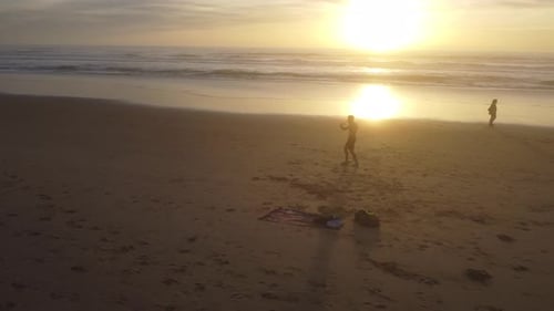 Dynamic drone shot of Man practicing Muay Thai on a beach, with the sunset as a background.