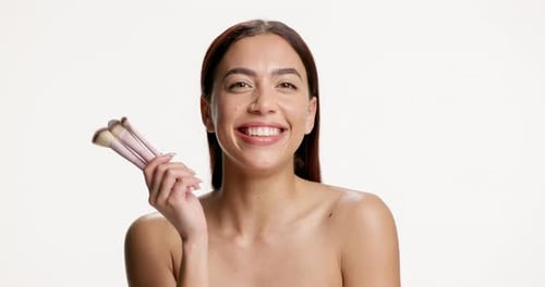 Face, makeup brushes and happy woman in studio for beauty, foundation product or self care
