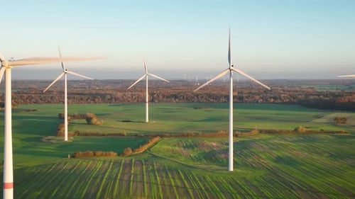 Aerial footage of wind turbines gracefully spin, one up close and lush forests landscapes provide th