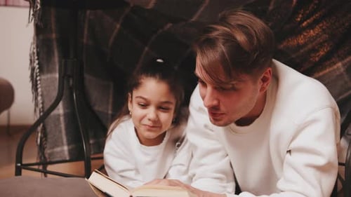 Man and Girl Read Stories Together Inside a Blanket Fort in a Cozy Room During an Evening at Home