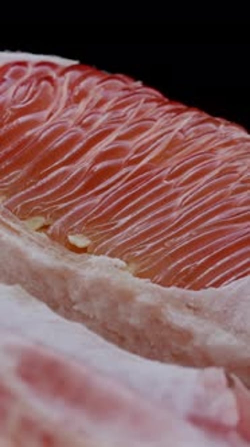 Vertical video. Half of a pomelo rotates on a black background, showcasing the red veins.