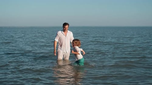 Father and Son Spray Each Other with Water While Swimming in the Ocean
