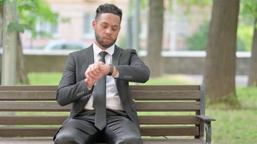 Man Checking Time on Watch on Park Bench