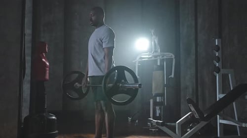 Man Lifts Barbell in Dramatic Gym Setting