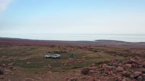 Aerial view of camping with tent and off-road vehicles on rocky valley with mountains along horizon