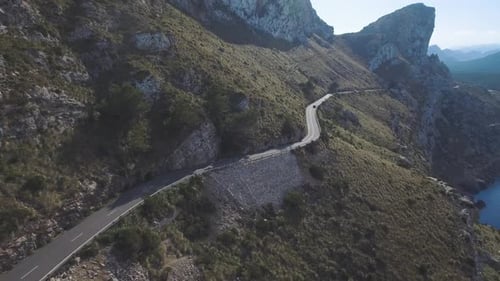 Breathtaking aerial footage in 4k of a car driving through the mountains on a small serpentine road