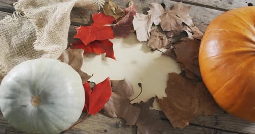 Paper with copy space against autumn leaves and pumpkins on wooden surface